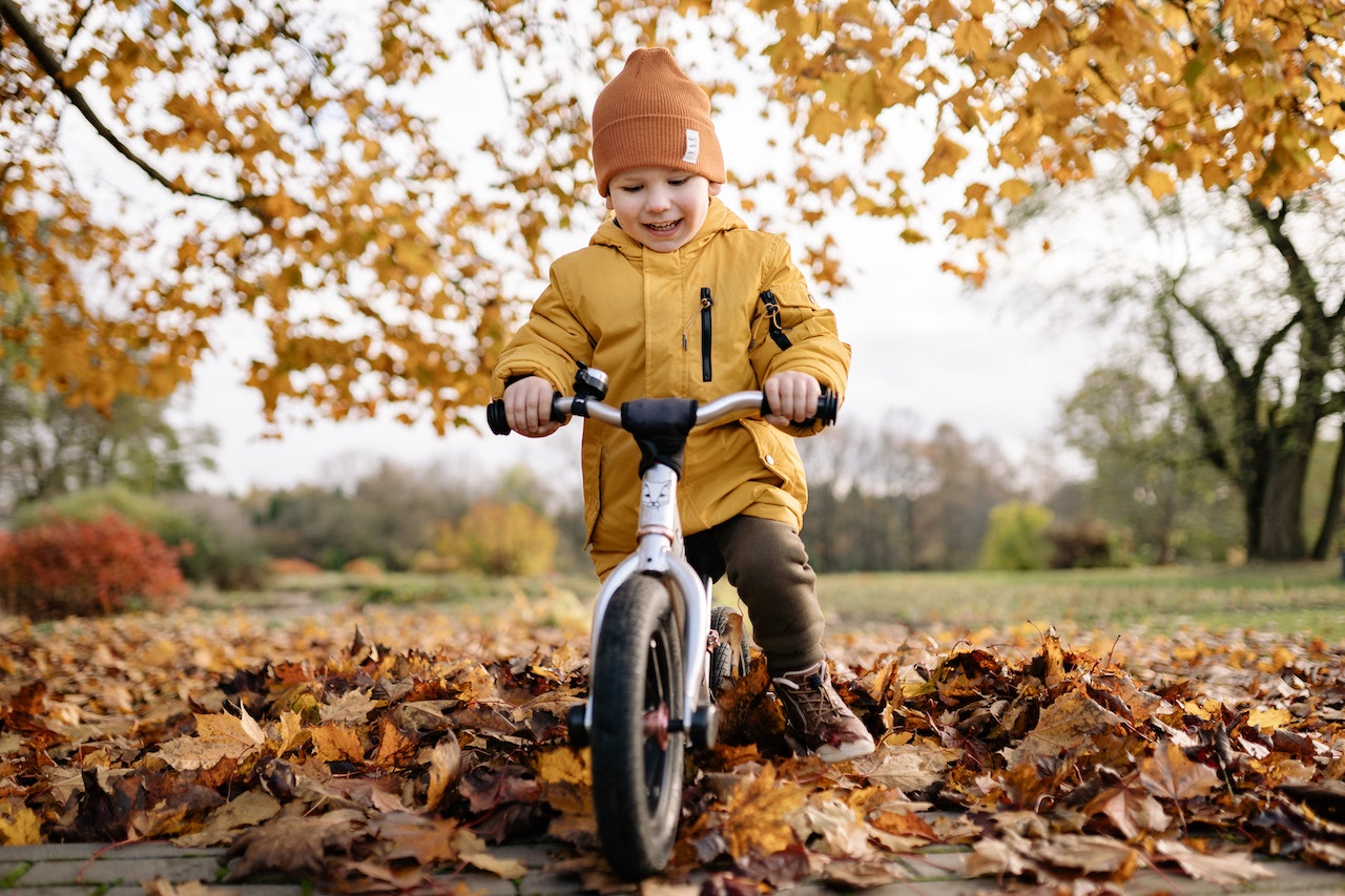 jesień, dziecko na rowerku w czapce i kurtce